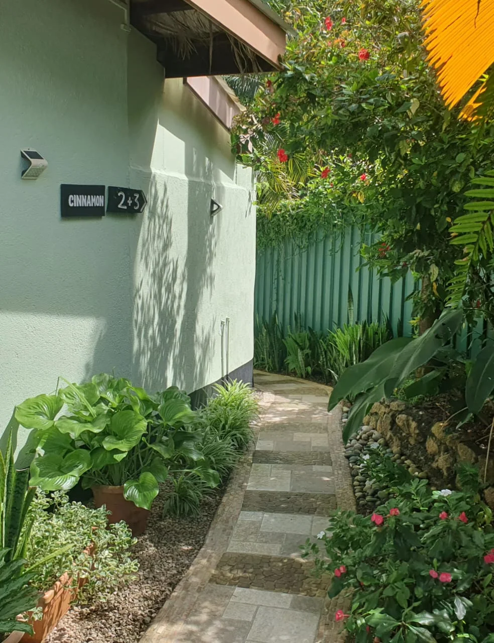 Sun-dappled tropical garden path with Cinnamon 2 + 3 signage and flowering shrubs — entrance to Garden Suite 2 at Maison Soleil at Maison Soleil, Anse Soleil, Seychelles