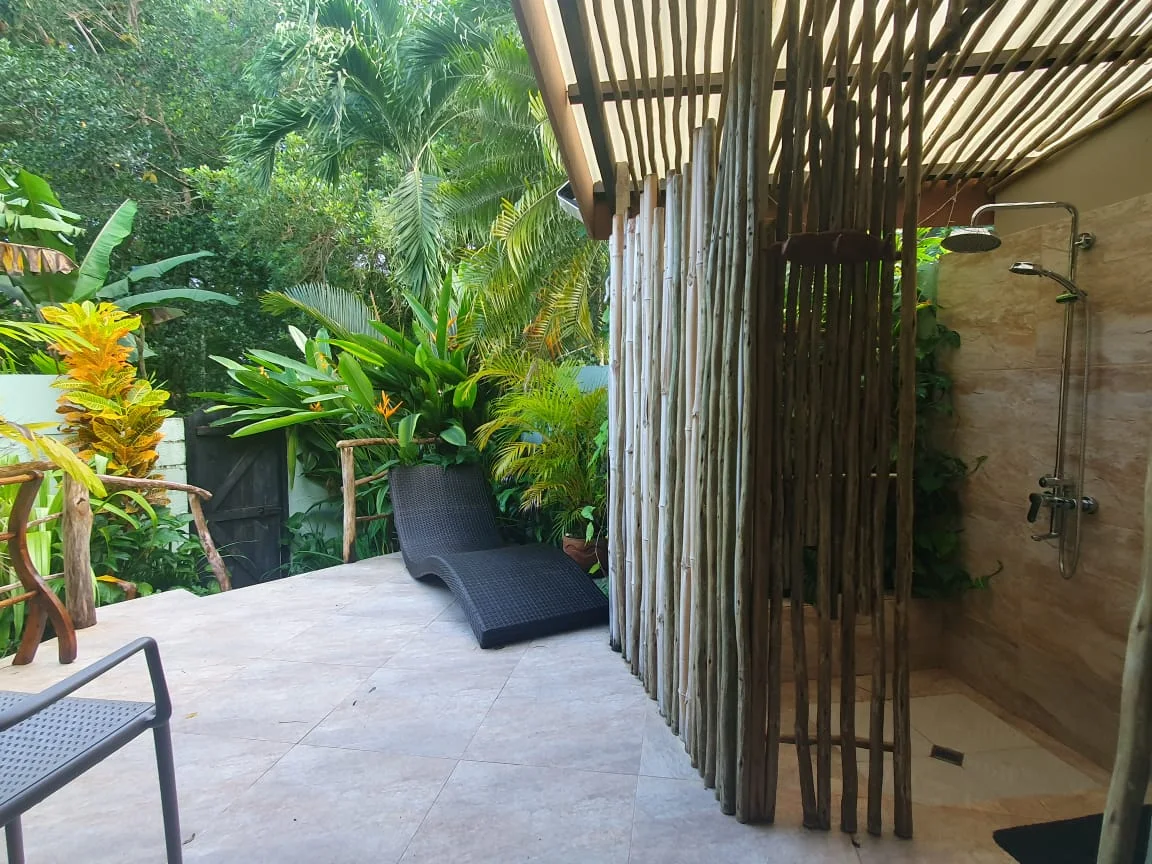 Private outdoor rain shower with natural wood privacy screen and wicker lounger on a tiled patio — Garden Suite 2 walled garden at Maison Soleil, Anse Soleil, Seychelles