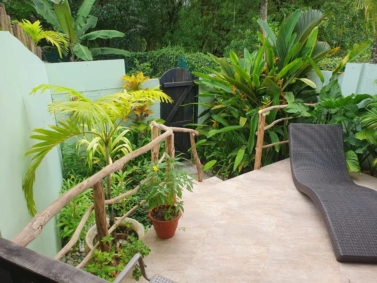 Private terrace with wicker sun lounger, lime-green walls and heliconia flowers — Garden Suite 2 at Maison Soleil, Anse Soleil, Seychelles