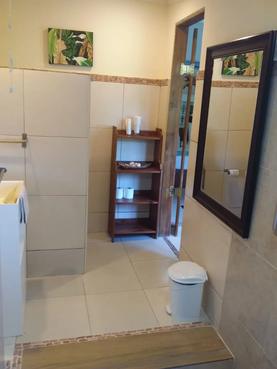 Tiled ensuite bathroom with dark wood shelving, framed mirror and tropical leaf artwork — Garden Suite 3 at Maison Soleil, Anse Soleil, Seychelles