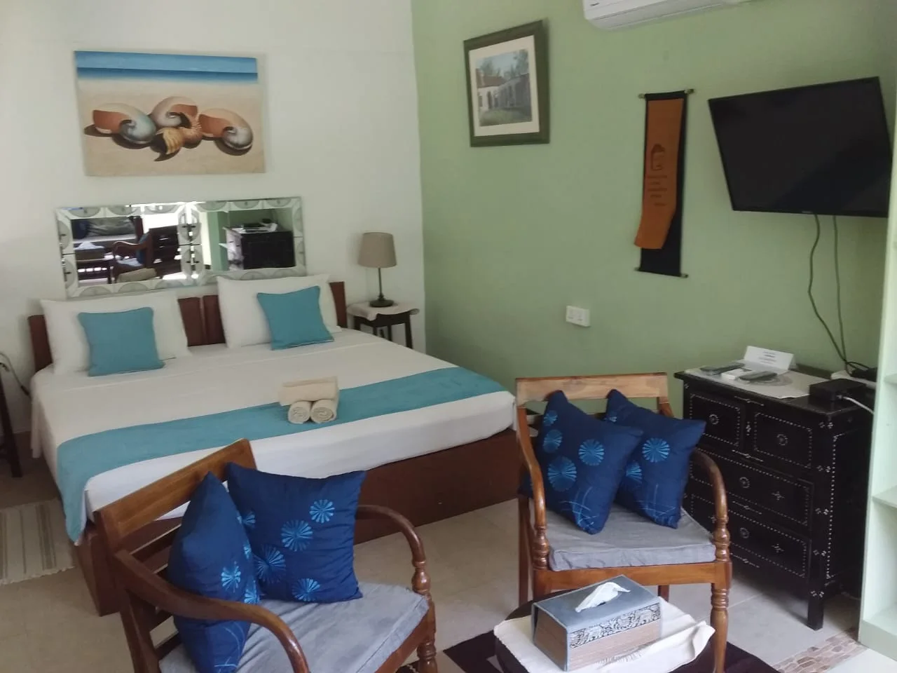 Bedroom with wooden armchairs, ornate dresser, turquoise bedding and seashell wall art — Garden Suite 3 at Maison Soleil, Anse Soleil, Seychelles