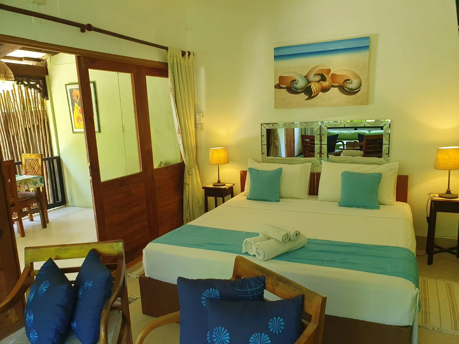 Bedroom with white and turquoise linens, seashell artwork and sliding doors opening to a private veranda — Garden Suite 3 at Maison Soleil, Anse Soleil, Seychelles
