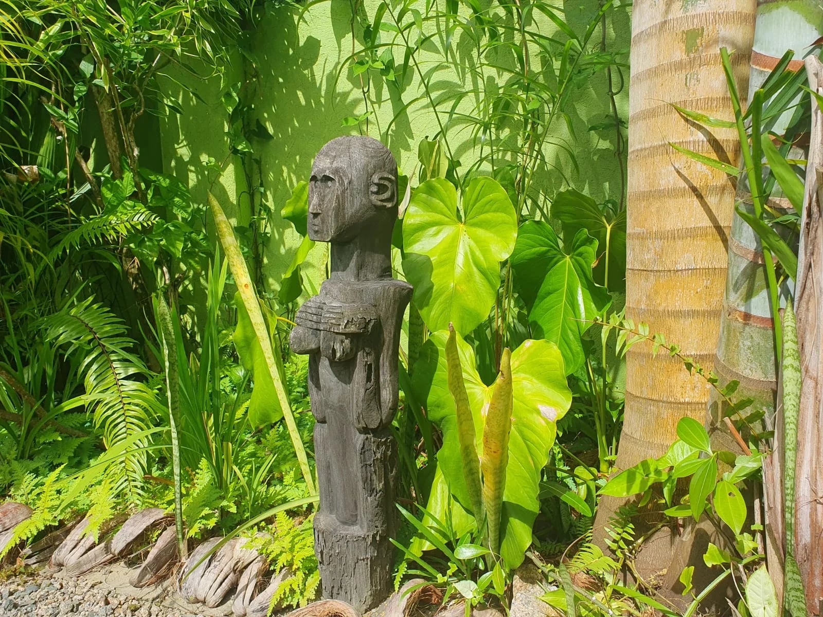 Hand-carved wooden statue among ferns and tropical plants in the garden — Andrew Gee retreat grounds at Maison Soleil, Anse Soleil, Seychelles